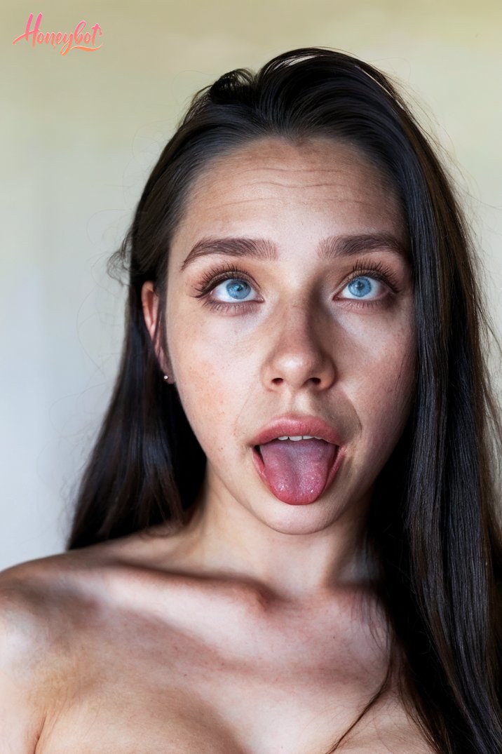 The image shows a woman with long dark hair. She appears to be making a playful expression by sticking out her tongue. The focus is on her face and upper body, showing her shoulde…